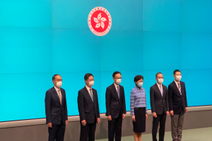 Eine Gruppe maskierter Individuen, die nebeneinander vor einer blauen Wand mit einem Logo stehen und an einer Pressekonferenz in Hong Kong teilnehmen.