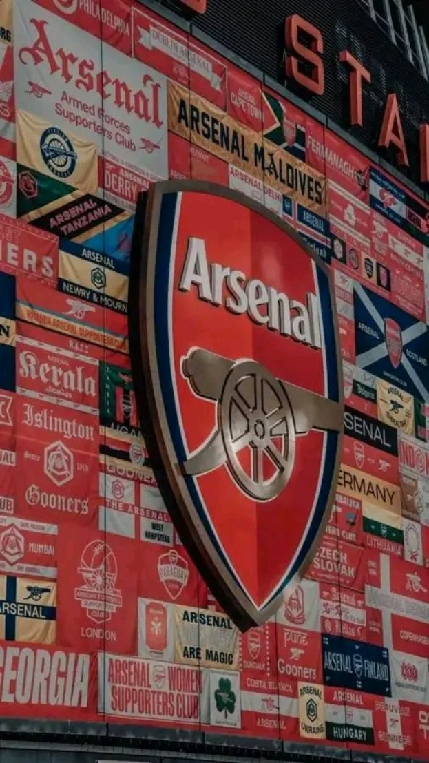 Arsenal FC-Logo auf der Seite eines Gebäudes mit Textbannern und Fahnen sowie Texttafeln unten.
