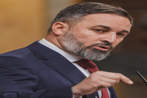 Ein Mann im Anzug und mit Krawatte spricht in ein Mikrofon und hält eine Rede mit einem unscharfen Hintergrund.