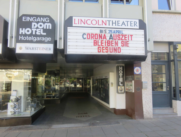 Das Lincoln Theater in Berlin, Deutschland, ein modernes Gebäude mit Glasfenstern und -türen, das eine Texttafel außen und ein geschäftiges Inneres mit verschiedenen Gegenständen zeigt.
