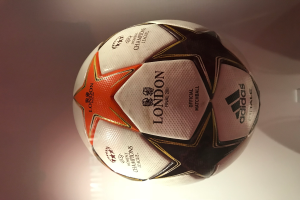 Ein weißer, schwarzer, oranger und roter Adidas-Fußball liegt auf einem weißen Tisch.