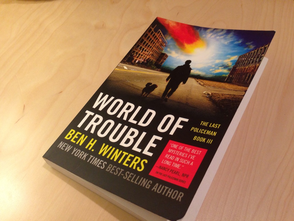 Ein Buch mit dem Titel "World Of Trouble" mit einem Mann und einem Hund auf dem Cover, das auf einem Tisch liegt.