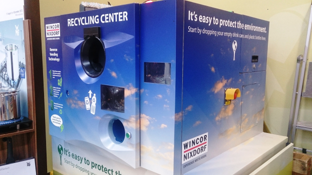 Ein blaues Recycling-Zentrum mit einer Tafel in der Mitte, einem Regal mit verschiedenen Gegenständen links und einem Gegenstand auf dem Boden rechts, mit Lampen und einer Wand im Hintergrund.