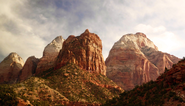Zion National Park in Utah mit majestätischen Bergen, grünen Bäumen, steinigem Gelände und einem Himmel voller weißer Wolken.