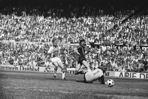 Schwarzes und weißes Foto von Fussballspielern auf einem Feld während eines Bundesliga-Spiels zwischen Ajax und Hannover 96 in der Saison 1978-79, mit Zuschauern im Hintergrund.