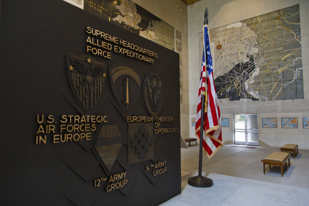 Eingang zum U.S. Strategic Air Forces Headquarters in Europa, mit einer amerikanischen Flagge, einer Wand mit Text und Logos, Bänken, einer Tafel, Fotorahmen und einer Tür im Hintergrund.