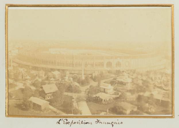 Schwarzes und weißes Foto eines Stadions in einer städtischen Umgebung, umgeben von Gebäuden, Bäumen und Strommasten, mit Text unten.