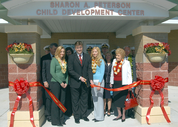 Gruppe von Menschen vor dem Sharon A Peterson Child Development Center, einige mit Kränzen, Bänder an Säulen und Topfpflanzen links und rechts vom Eingang.