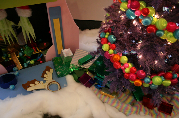 Drinnen, ein geschmückter Weihnachtsbaum rechts, Geschenkboxen und Dekorationen in der Mitte, eine Hütte mit Dekorationen oben links und Stoffe unten.