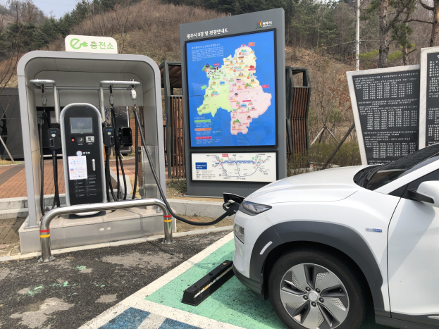 Ein Elektroauto, das an einer Ladestation in Seoul, Südkorea, geladen wird, mit Bäumen und Himmel im Hintergrund.