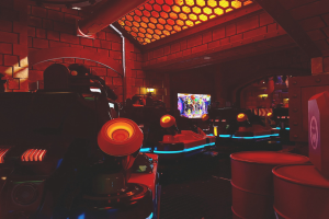 Ein hell erleuchteter Raum voller verschiedener Arcade-Videospielautomaten, Bildschirme und Gegenstände, einschließlich einer sichtbaren Rohrleitung und Deckenlampen.