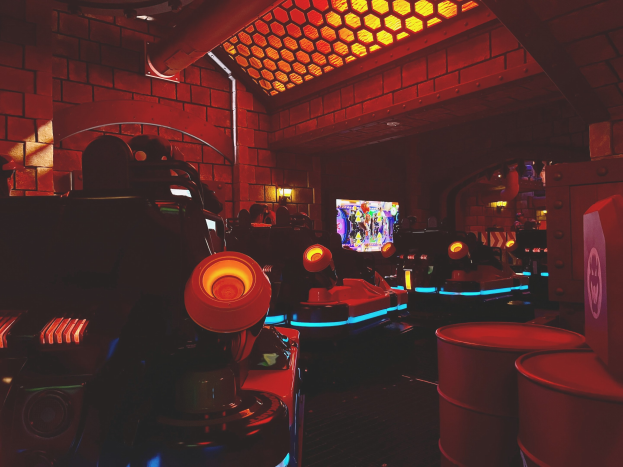 Ein hell erleuchteter Raum voller verschiedener Arcade-Videospielautomaten, Bildschirme und Gegenstände, einschließlich einer sichtbaren Rohrleitung und Deckenlampen.