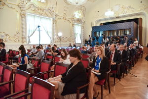 Eine große Gruppe von Menschen sitzt in Stühlen in einem Raum mit einer Wand, Fenstern mit Vorhängen, Lichtstativen und Kronleuchtern an der Decke, einige halten Kameras und besuchen eine Pressekonferenz in Moskau.