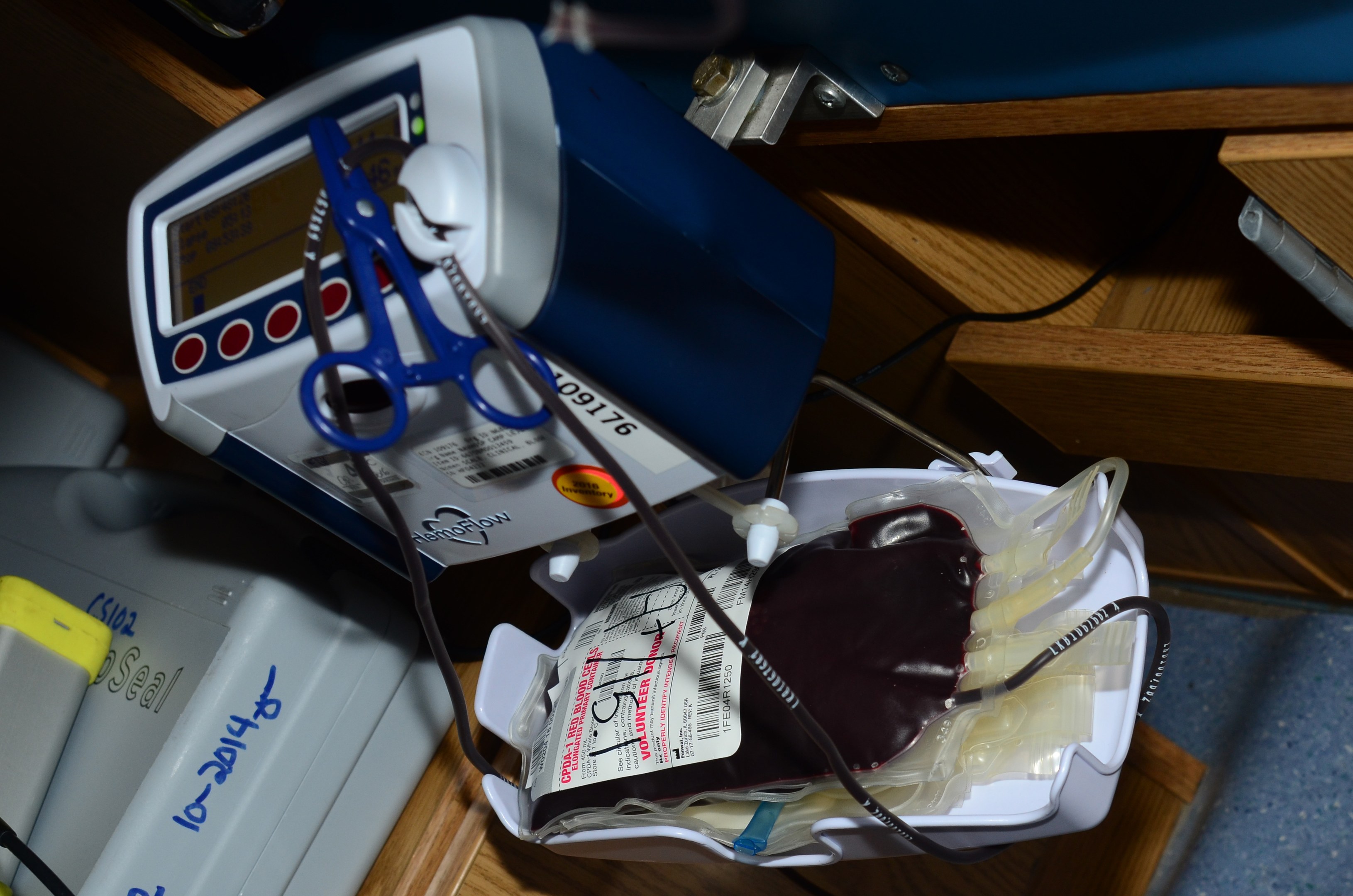 Blutdruckmessgerät auf einem Holztisch neben einer Schere, mit einem elektronischen Gerät und Kabeln links und zusätzlichen Gegenständen rechts.