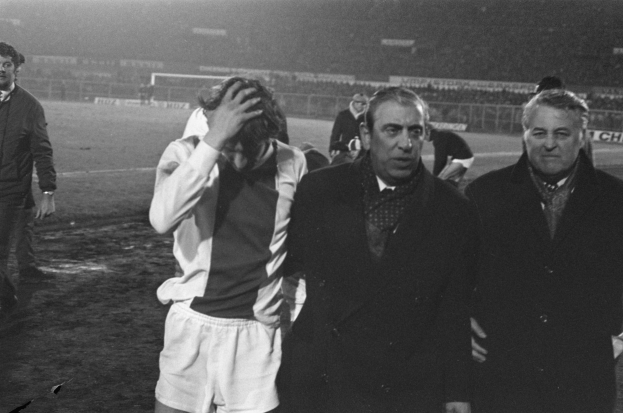 Schwarzes und weißes Bild einer Gruppe von Männern, die auf einem Fußballfeld stehen und ein Stadion im Hintergrund sehen, die enttäuscht nach einem Sieg aussehen.