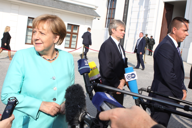 Bundeskanzlerin Angela Merkel spricht mit Reportern vor dem Kanzleramt in Berlin, umgeben von einer Gruppe von Menschen mit Mikrofonen und Gebäuden im Hintergrund.