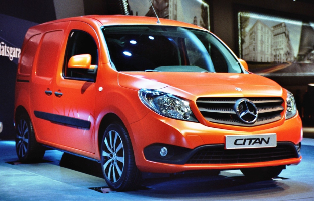 Orange Mercedes-Benz Citan Lieferwagen zwischen schwarzen Schlafzimmer-Möbelsets auf einer Autauschstellung gezeigt.