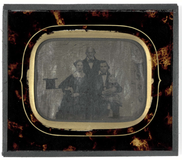 Schwarzes-Weiß-Foto eines Mannes in Anzug und Krawatte und einer Frau in unbekannter Kleidung vor einem Fernseher stehend, beide mit ernsten Gesichtern.