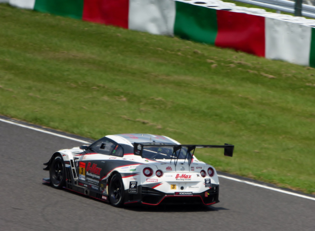 Ein Nissan GT-R Nismo GT3 Rennwagen auf der Nürburgring 24 Stunden Rennstrecke, mit grünem Gras und einem Zaun im Hintergrund.
