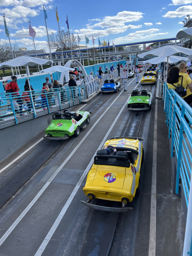 Menschen auf einer Achterbahn in Disney's Hollywood Studios, umgeben von Geländern, Fahnen, Bäumen und Gebäuden unter einem bewölkten Himmel.